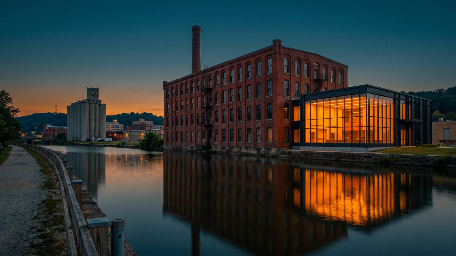 A historic Akron brick factory with a modern glass laboratory addition beside a canal towpath at blue hour